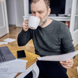 Employé en télétravail, buvant un café et lisant un dossier